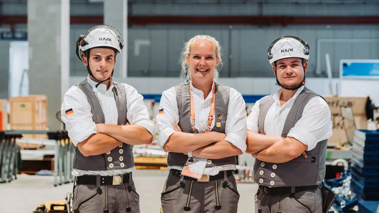 Betonbaumeisterin Jule Janson posiert in einer Werkhalle zwischen Tim Arnold und Jakob Distler.